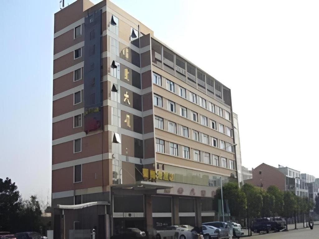 a tall building with cars parked in a parking lot at Nantong GuoDu Hotel in Nantong