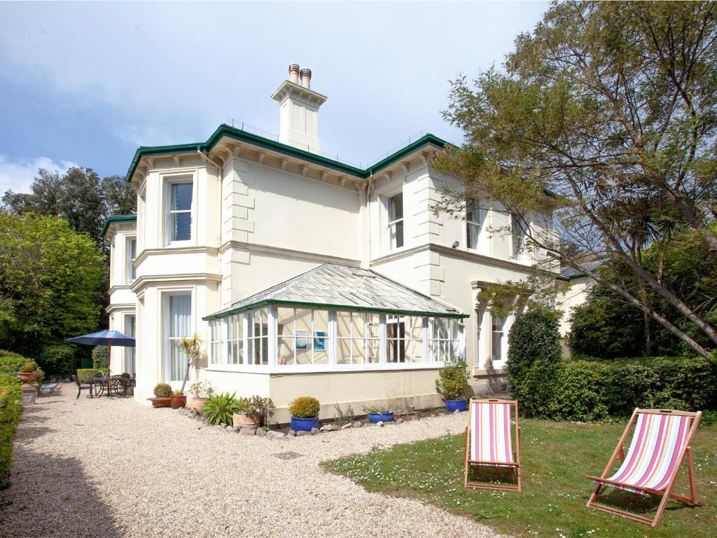 a large white house with two lawn chairs in the yard at Longcroft House in Torquay