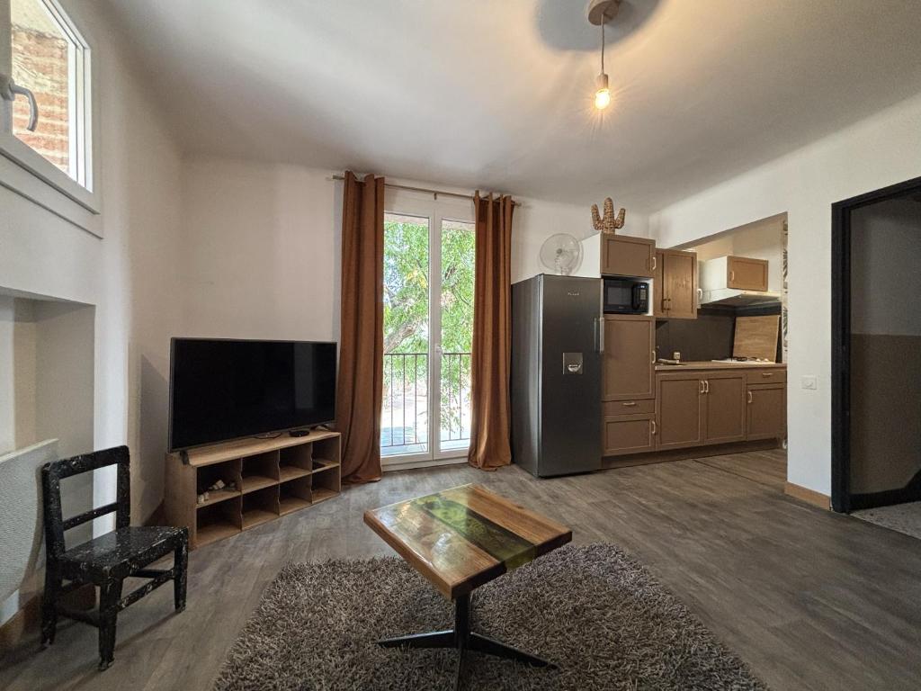 ein Wohnzimmer mit einem TV und einem Tisch sowie eine Küche in der Unterkunft Elégante Maison de Village in Ortaffa