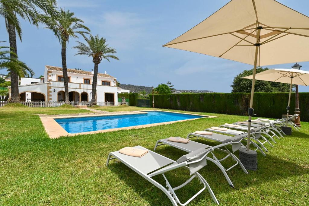 a group of lawn chairs with umbrellas and a pool at Riu Rau in Jávea