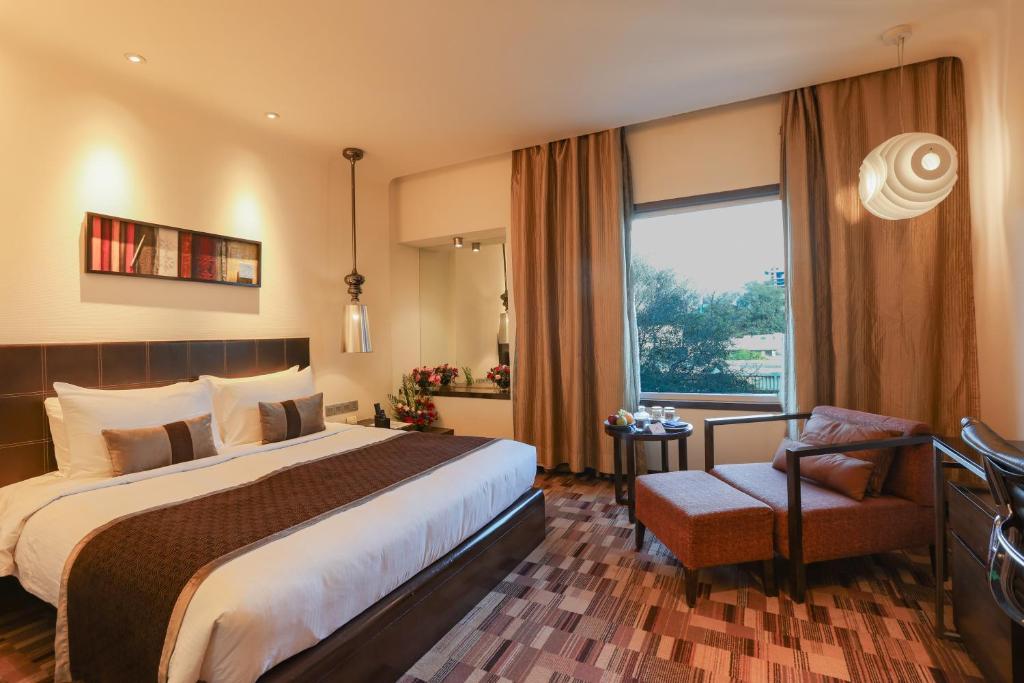 Una habitación de hotel con una cama, una silla y una ventana. en Pride Premier Pune, en Pune
