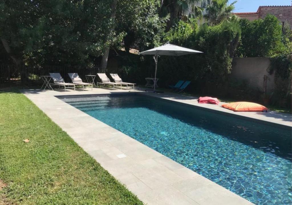 - une piscine avec des chaises et un parasol à côté d'une cour dans l'établissement Maison Traditionnelle Catalane avec terrain de tennis et piscine, à Palau-del-Vidre