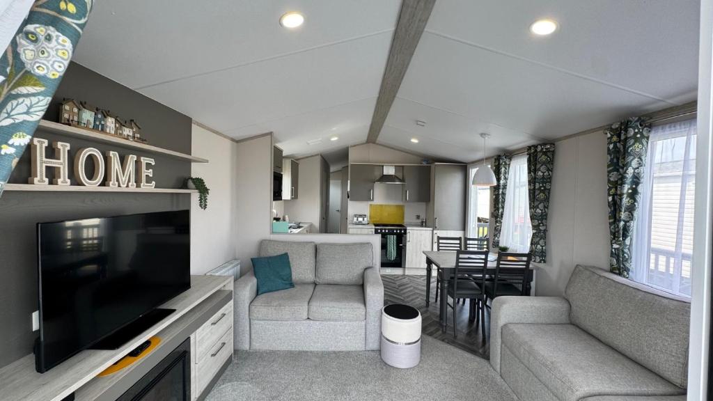 a living room with a tv and a couch and a kitchen at Pure Living -West Sands, Quiet Grassy retreat Seal Bay in Selsey