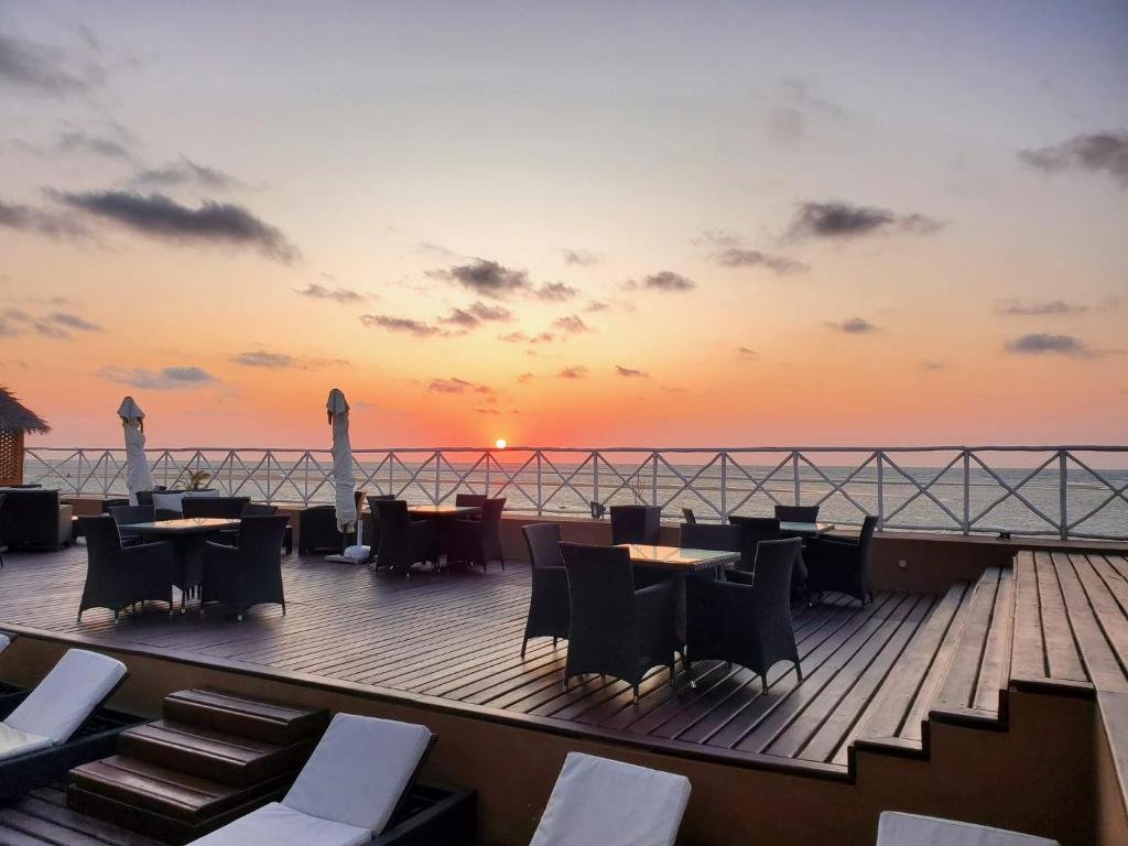 una terraza con mesas, sillas y una puesta de sol en VEZO BEACH HOTEL Morondava, en Morondava