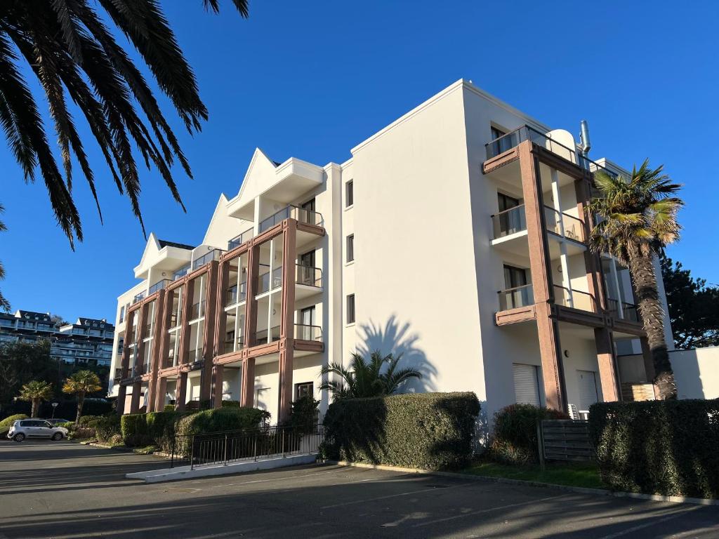 un bâtiment blanc avec des palmiers devant dans l'établissement Trestraou 217, à Perros-Guirec