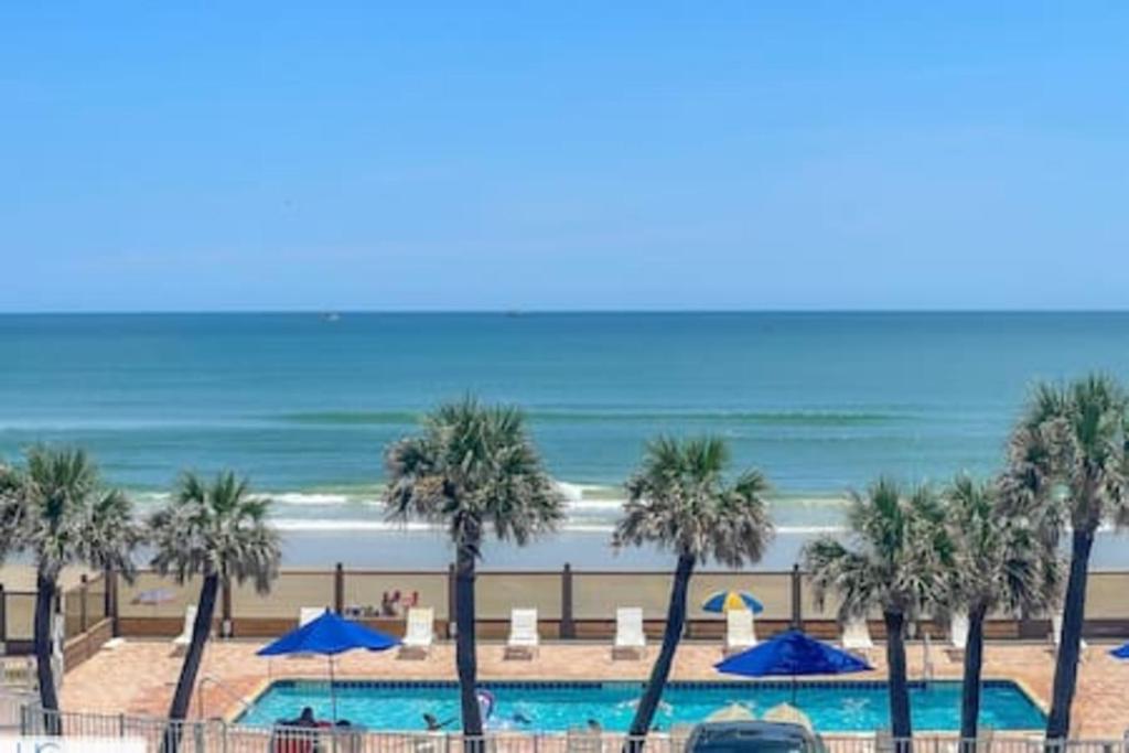 a pool with palm trees and blue umbrellas and the beach at Stylish Studio Ocean View in Daytona Beach