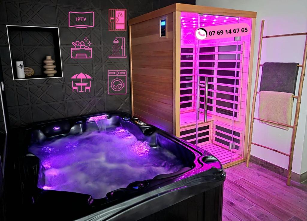 a hot tub in a room with pink lighting at Love Room Luxe and Spa - Sauna in Domérat