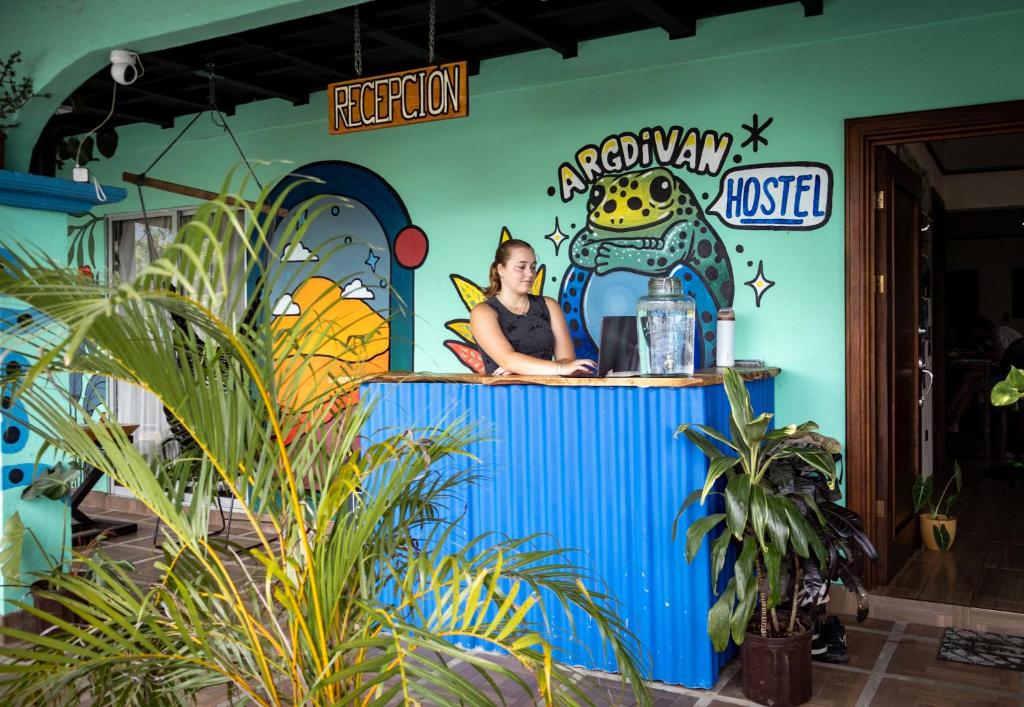 uma mulher sentada num balcão numa sala com plantas em Argdivan Hostel em Fortuna