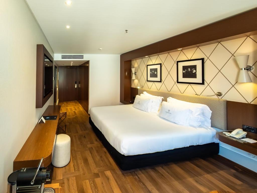 A large bedroom with a king-size-looking bed, desk, luggage space and decorative headboard.