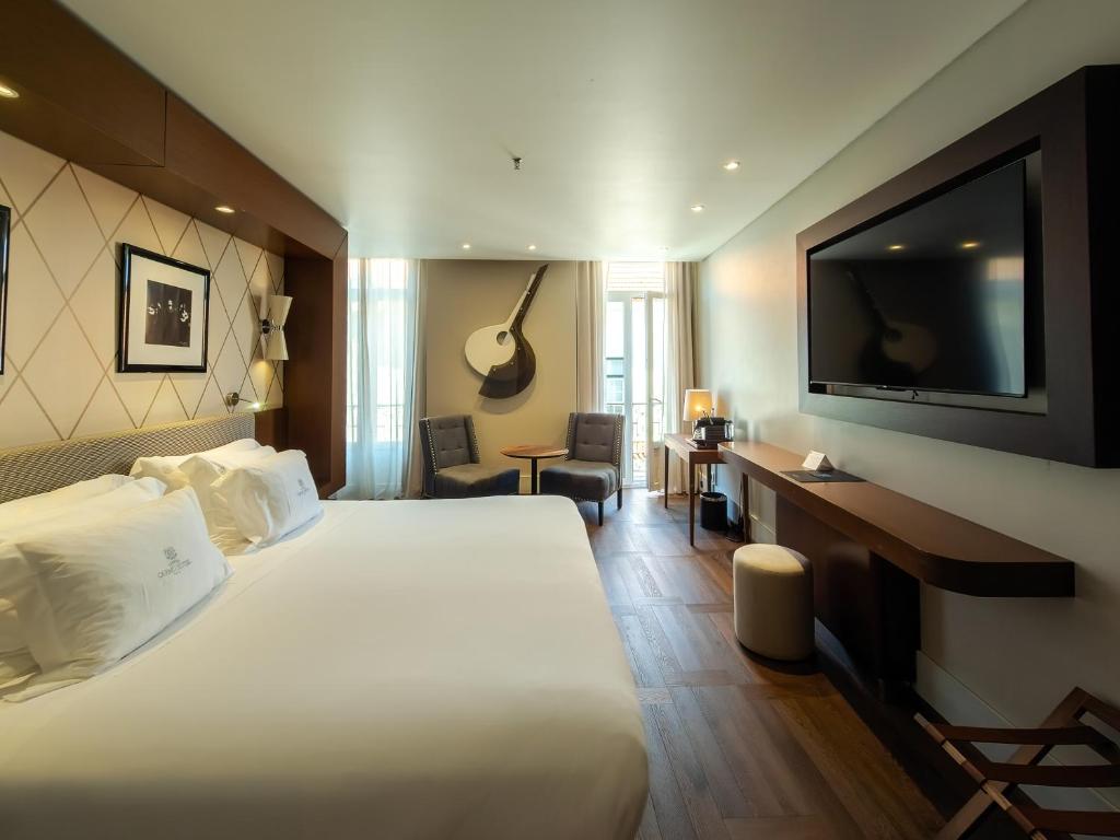 A bright double room with a large bed, television, desk and two lounge chairs.