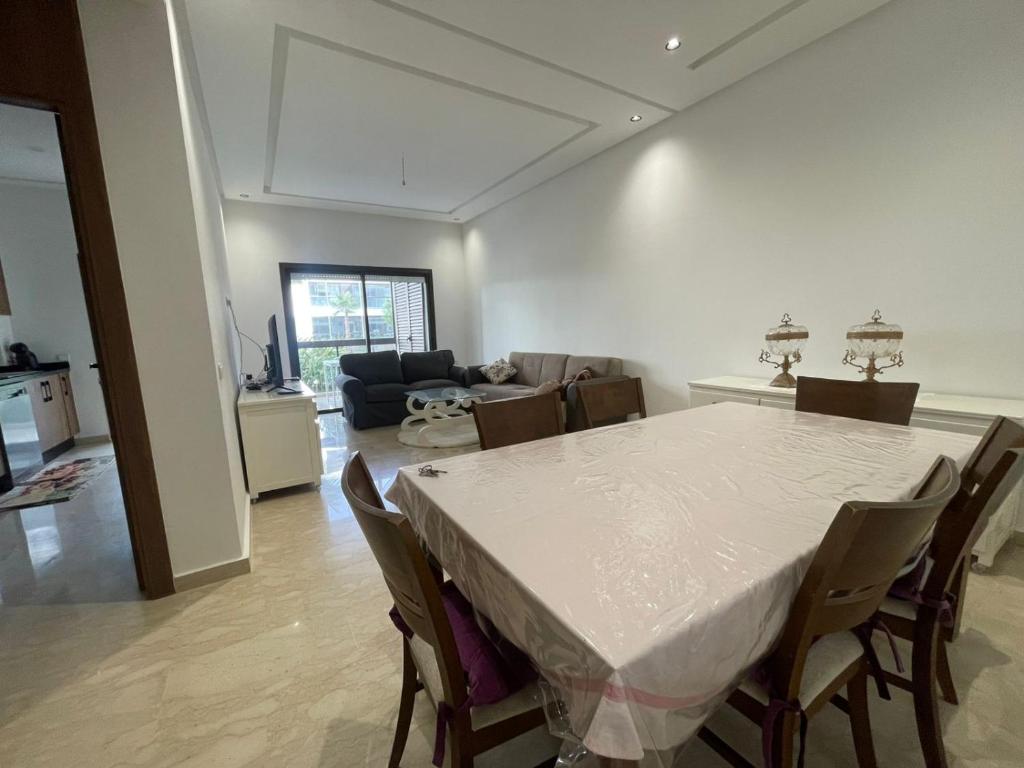 a dining room and living room with a table and chairs at Appartement Luxe Vue Piscine Résidence Les Perles de Bentriaa, El Mansouria in Mohammedia