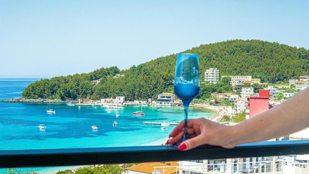 a person holding a blue wine glass overlooking a beach at Simon Ionian Balcony 1 - Kitchen, Sea View in Himare