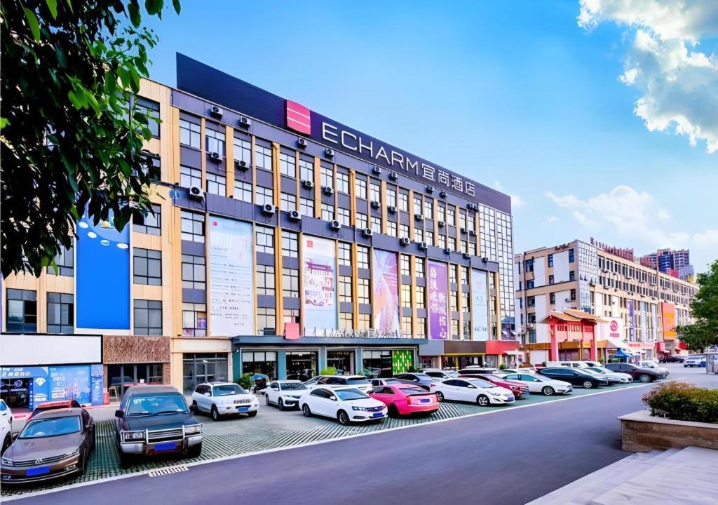 a large building with cars parked in a parking lot at Echarm Hotel Qianxi High Speed Railway Station in Qianxi
