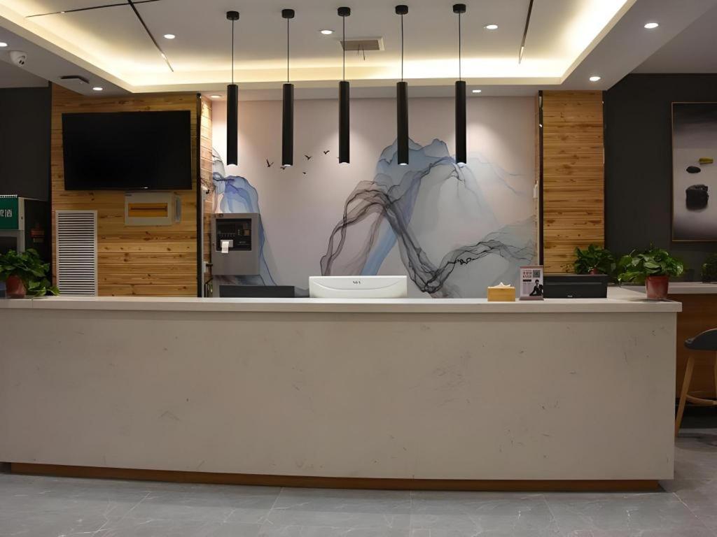 a lobby with a white counter with pendant lights at Shell Hotel Kaifeng Jin'an Road Bianxihu Wanda Plaza in Kaifeng