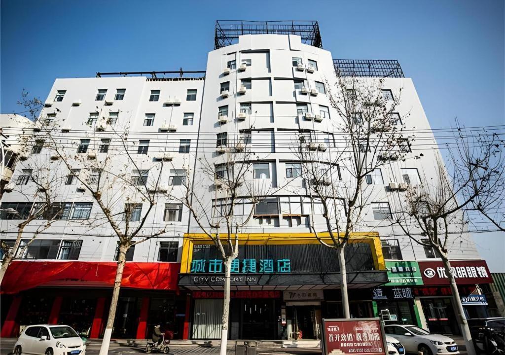 ein hohes weißes Gebäude mit Bäumen davor in der Unterkunft City Comfort Inn Fuyang Hongqi Middle School Erlijing Night Market in Fuyang