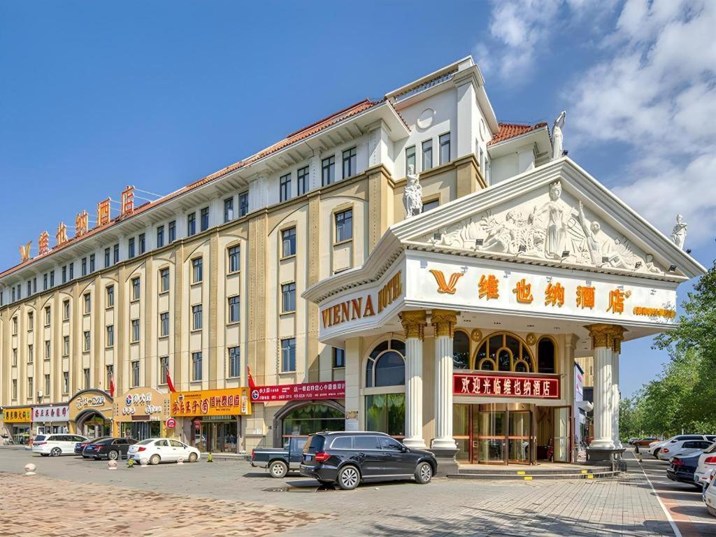 a large building with cars parked in front of it at Vienna Hotel Tianjin Huaming in Tianjin