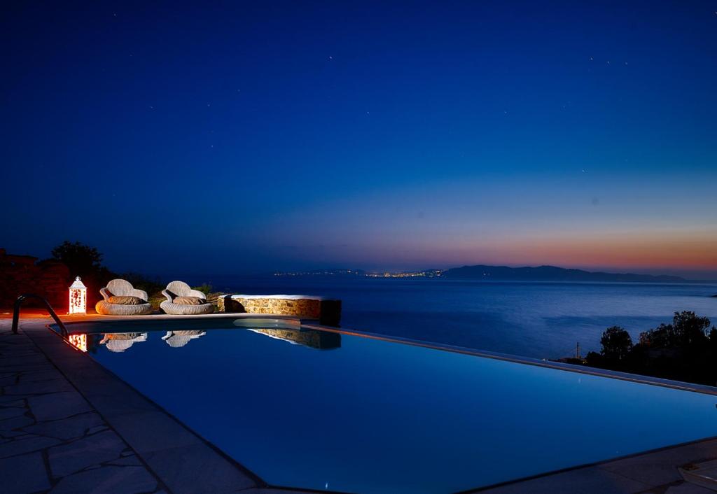 uma piscina com vista para o oceano à noite em Vega Apartments em Tinos