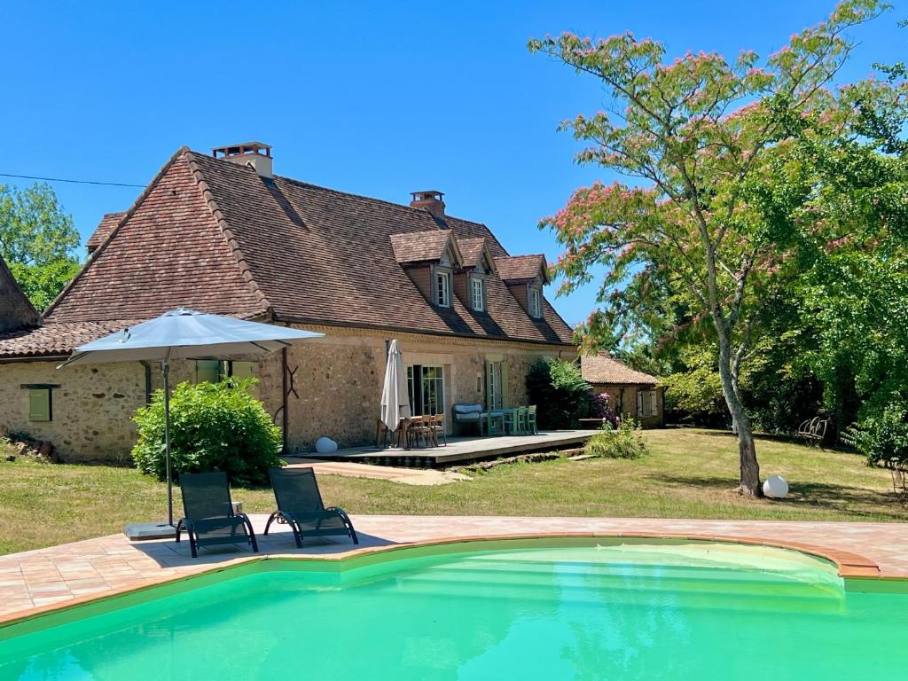 une maison avec une piscine, 2 chaises et un parasol dans l'établissement Belle maison ancienne en Perigord avec piscine, à Rouffignac-Saint-Cernin-de-Reilhac