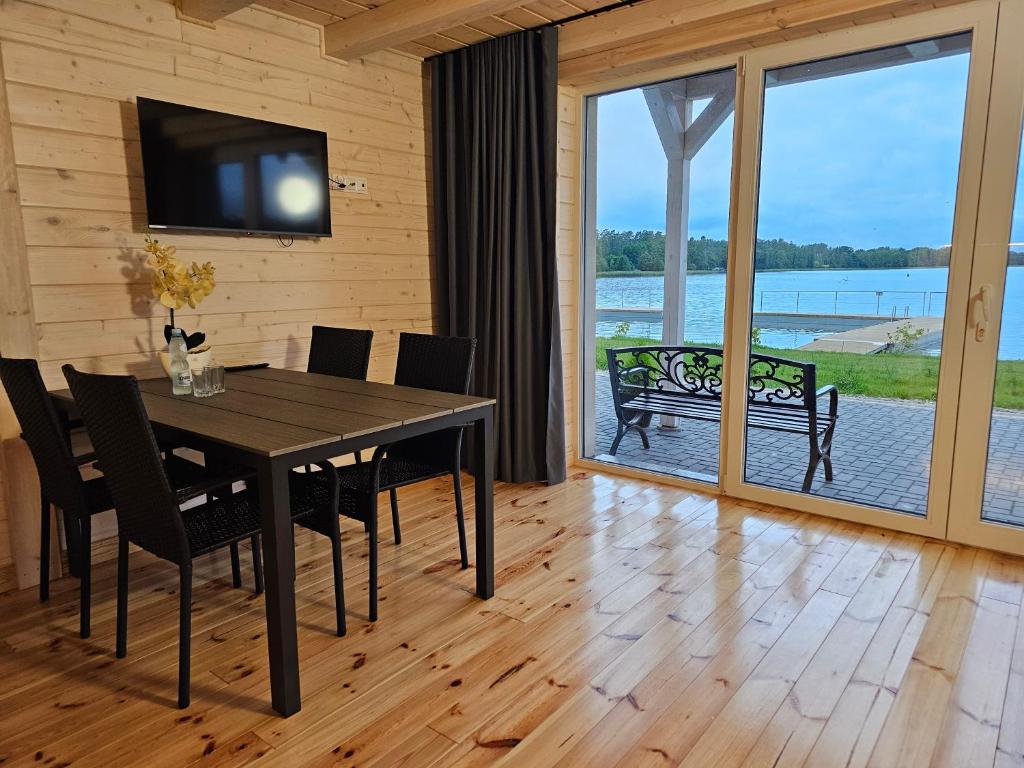 Wooden dining area with table, chairs, TV, and large window overlooking a lake.