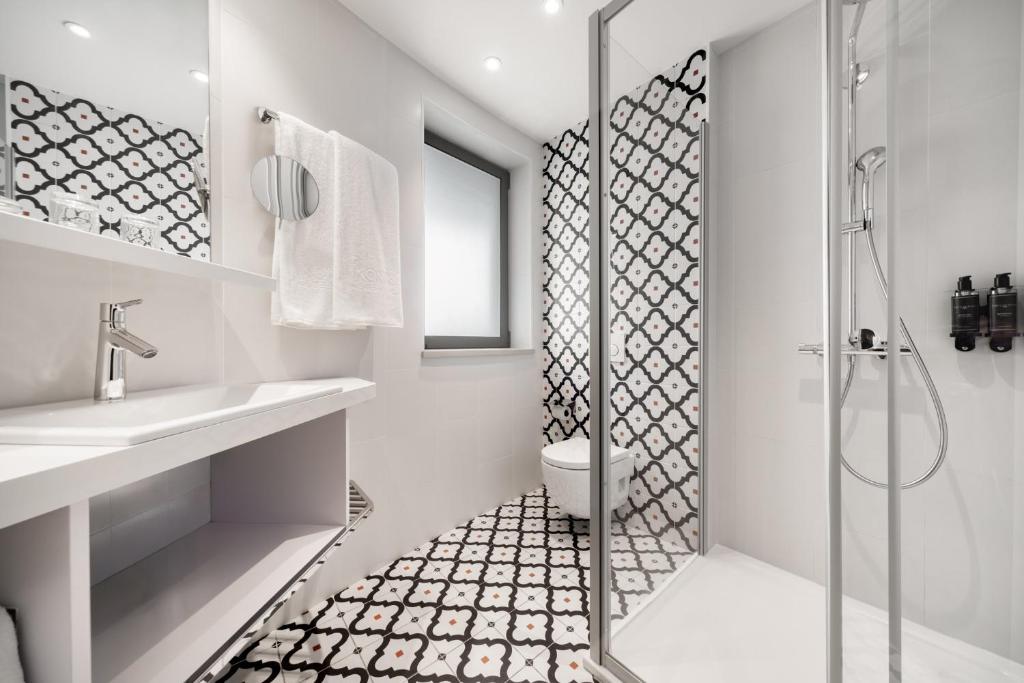 A compact tiled bathroom with a walk-in shower, toilet, and wall-mounted sink.
