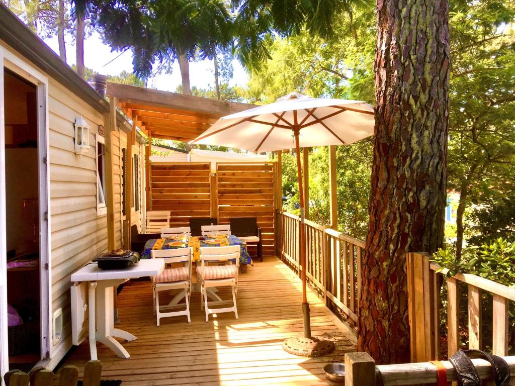 a wooden deck with a table and an umbrella at Charmant mobil home au Cap Ferret, idéalement situé dans un camping 4 étoiles Sibulu les Embruns à Claouey in Lège-Cap-Ferret
