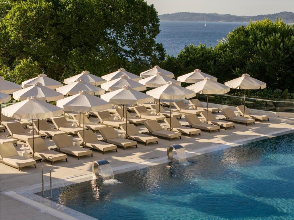 Eine Gruppe von Stühlen und Sonnenschirmen neben einem Schwimmbecken in der Unterkunft Valmar Corfu in Agios Ioannis Peristerion
