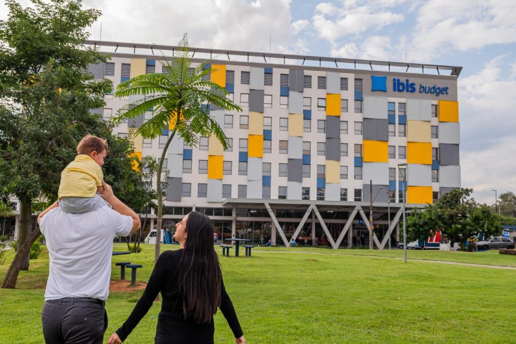 瓜鲁柳斯Ibis Budget Guarulhos Aeroporto的一名男子在建筑物前肩上抱着一个孩子
