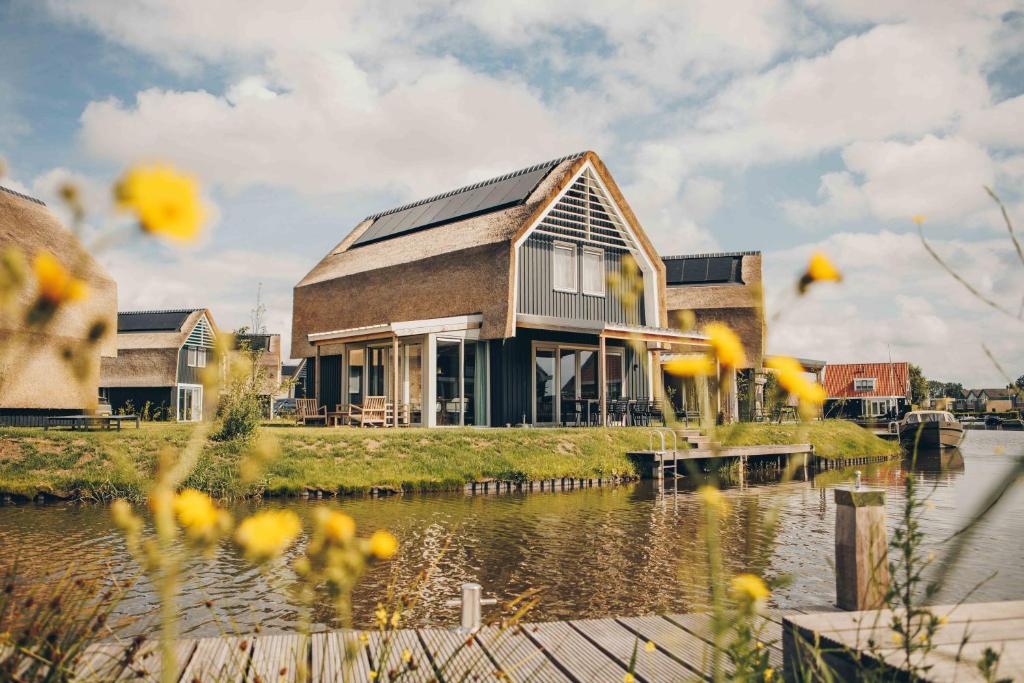 a house on the water with yellow flowers in the foreground at Watervilla binnenhaven met Sauna | 8 personen - Boutique Parc Pharshoeke in Heeg