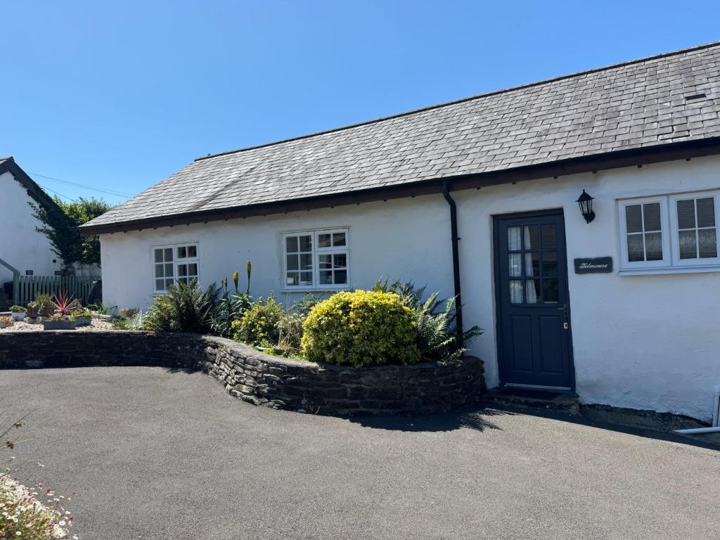 a white house with a black door in a driveway at Titmouse at Trenale Court Cottages in Tintagel