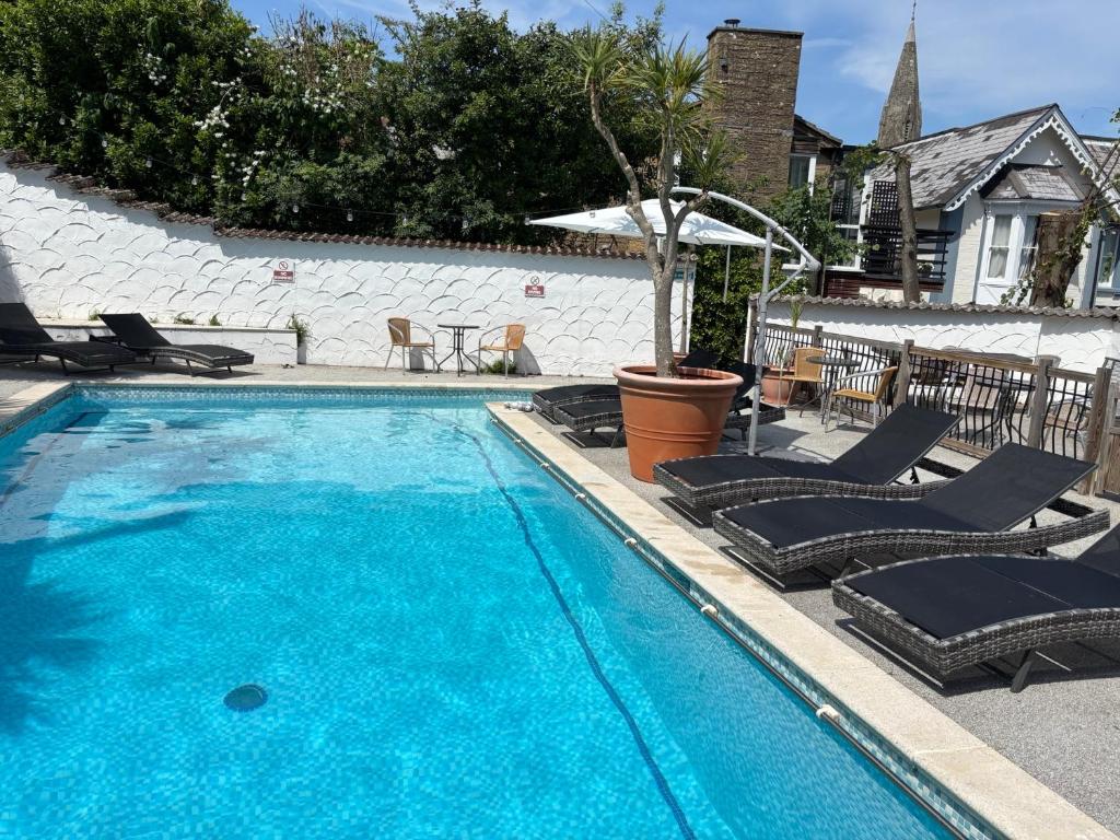 a blue swimming pool with chairs and a tree at The Havelock in Shanklin