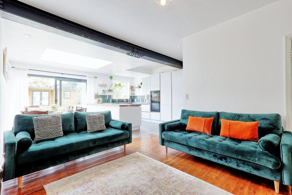 a living room with two green couches and orange pillows at Beautiful 5 bed house, relaxing garden and driveway parking 10 min to the beach in Southend-on-Sea
