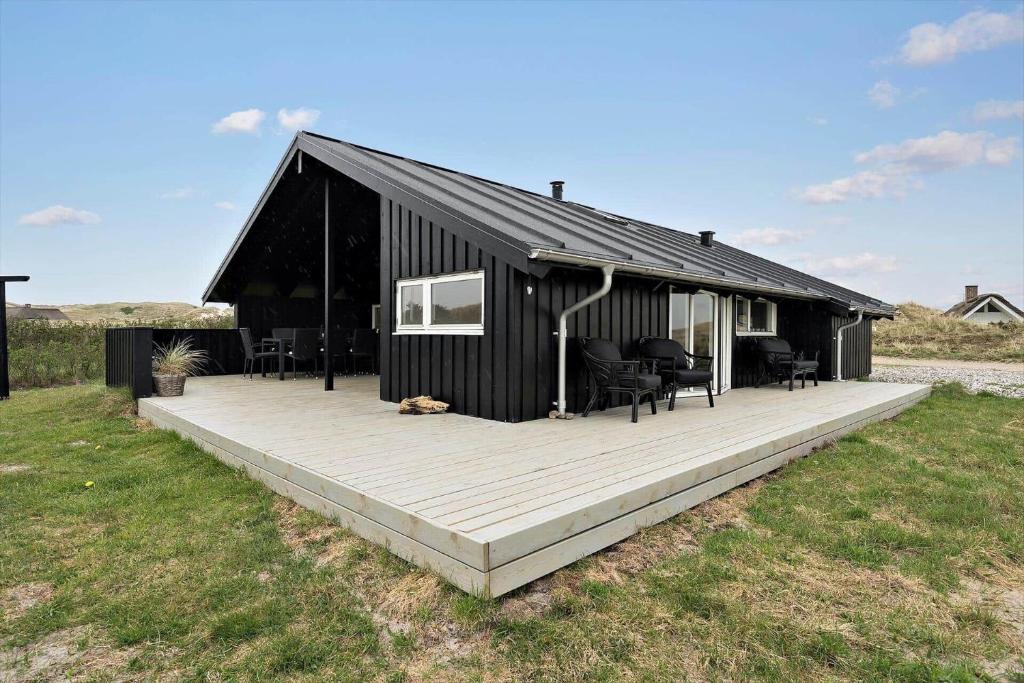 a black house with a wooden deck in a field at 090-Ringkobing-Klaegdalen-9 in Ringkøbing