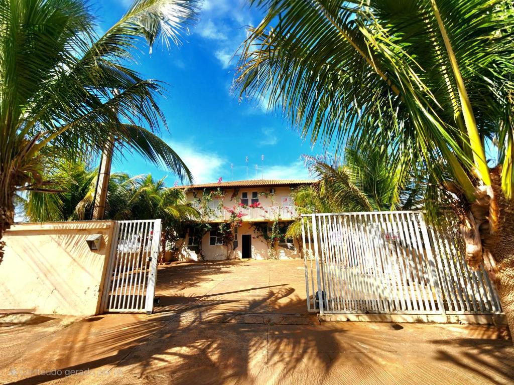 a white gate in front of a house with palm trees at Économique Hotel in Ilha Solteira