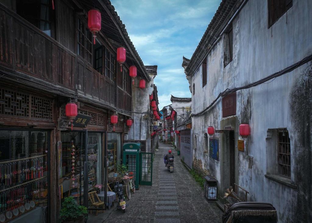 Ein Mann fährt mit einem Roller durch eine Gasse mit Gebäuden in der Unterkunft Hangzhou Tonglu Baobao Hotel in Tonglu