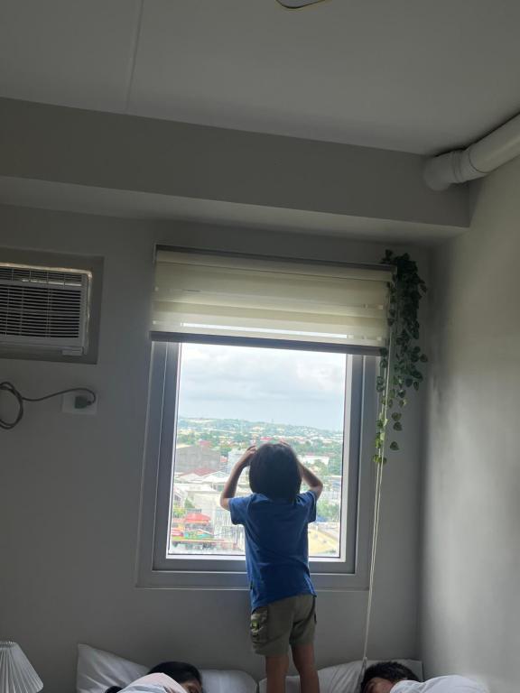 a young child is looking out of a window at Cozy 2BR Stay for 6pax in High-Floor, Wi-Fi & Family Games near IT Park Cebu- Unit Scarlett by GERRA in Mandaue City