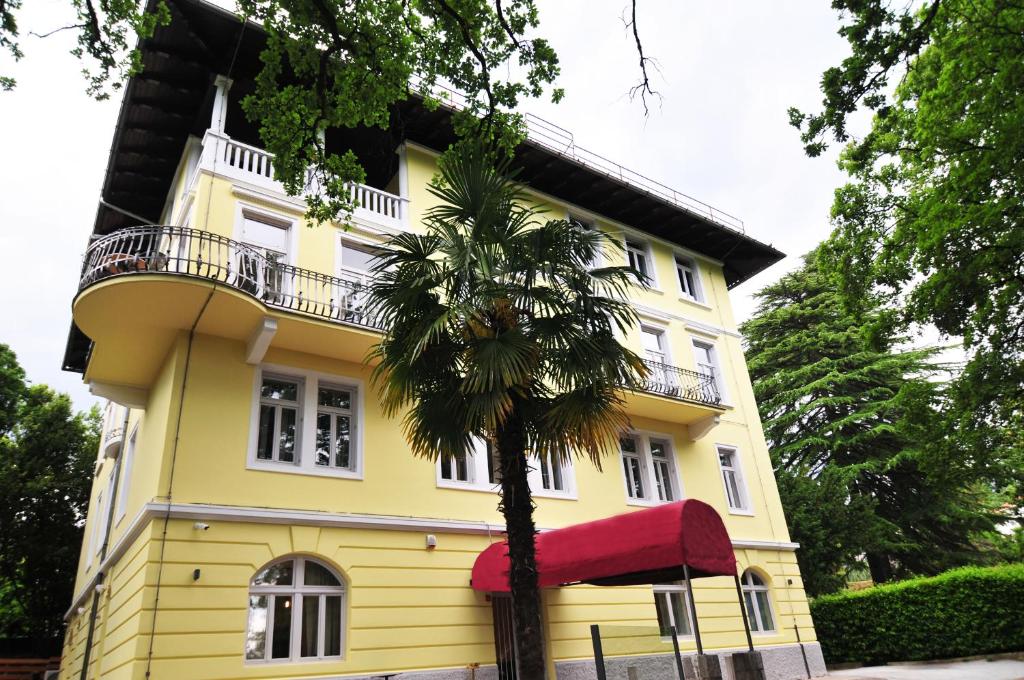 ein gelbes Haus mit einer Palme davor in der Unterkunft Hotel Villa Laurel in Lovran