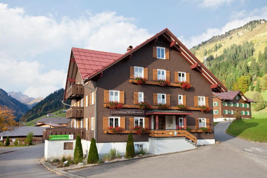 un grand bâtiment avec un toit rouge dans l'établissement Gästehaus Widderstein, à Mittelberg