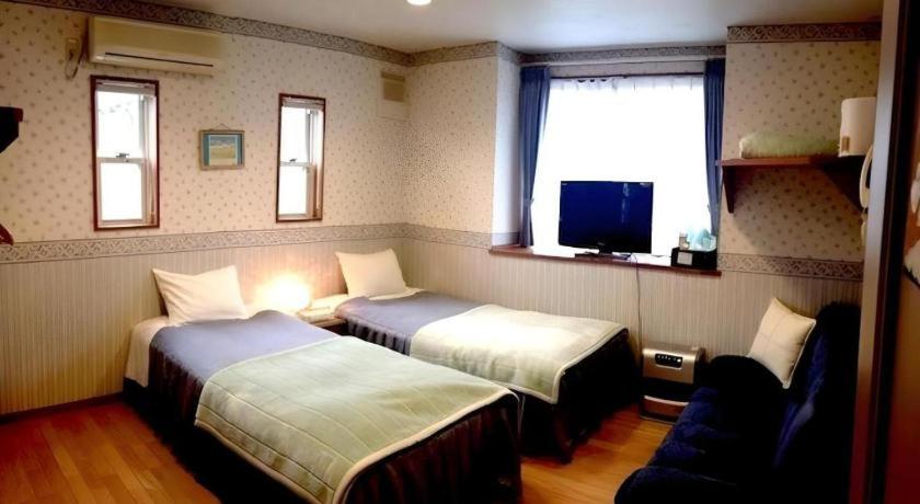 ein Hotelzimmer mit zwei Betten und einem Fernseher in der Unterkunft Pension Twilight in Nasu-yumoto