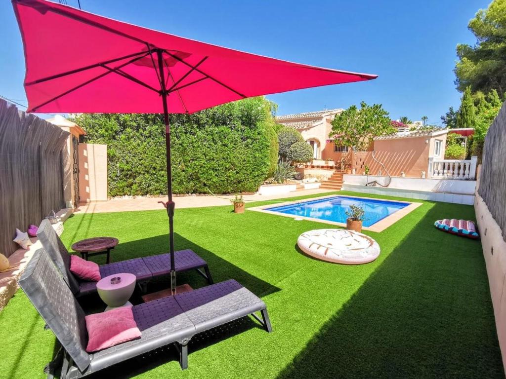 a yard with a red umbrella and chairs and a pool at Villa Tossalet VYB in El Tosalet