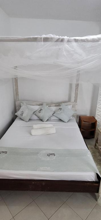 a bed with white sheets and pillows on it at L & C Chinese Studio in Diani Beach