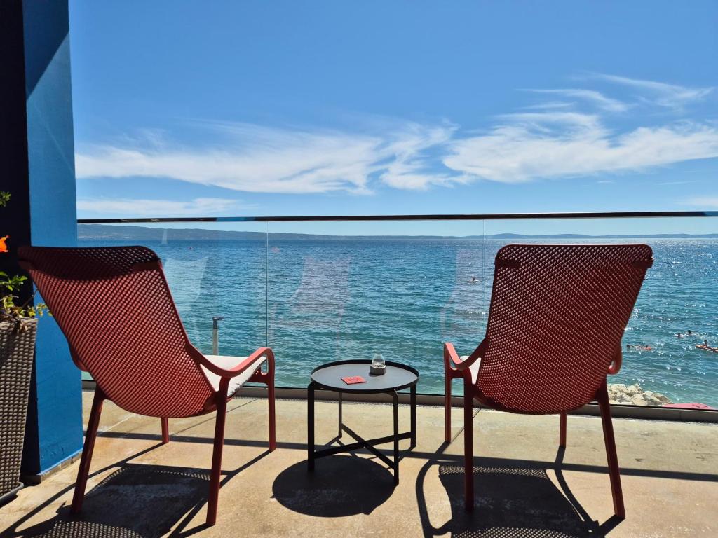 two chairs and a table on a balcony with the ocean at Beachfront Apartments Zanic in Podstrana
