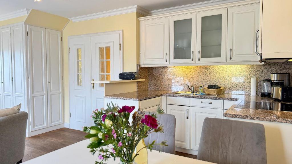 a kitchen with white cabinets and a vase of flowers on a table at Syltrose Whg 1b in Westerland (Sylt)