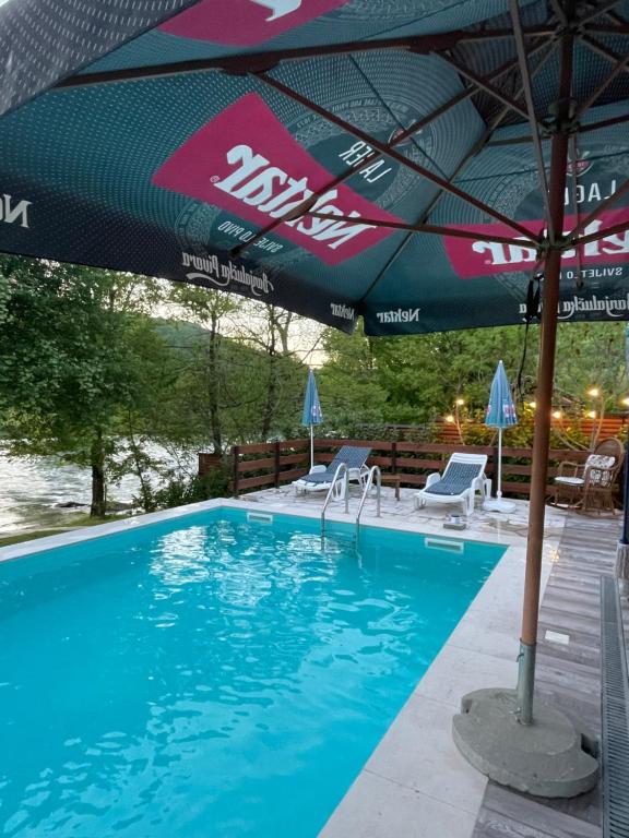 a swimming pool with an umbrella and chairs at Property with your own beach and pool - Whispering Waters in Krupa na Vrbasu