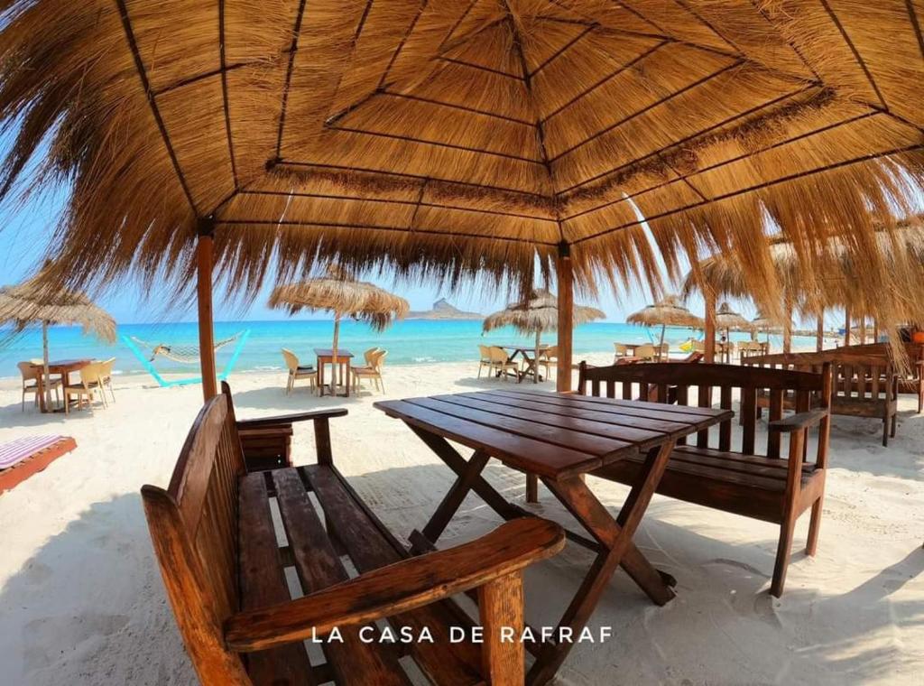 a picnic table on the beach with chairs and umbrellas at Casa del Mar Rafraf in Rafrāf