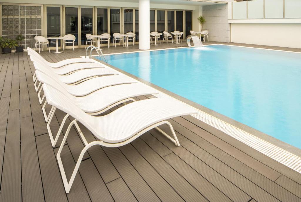 a group of white lounge chairs next to a swimming pool at NH Coimbra Dona Ines in Coimbra