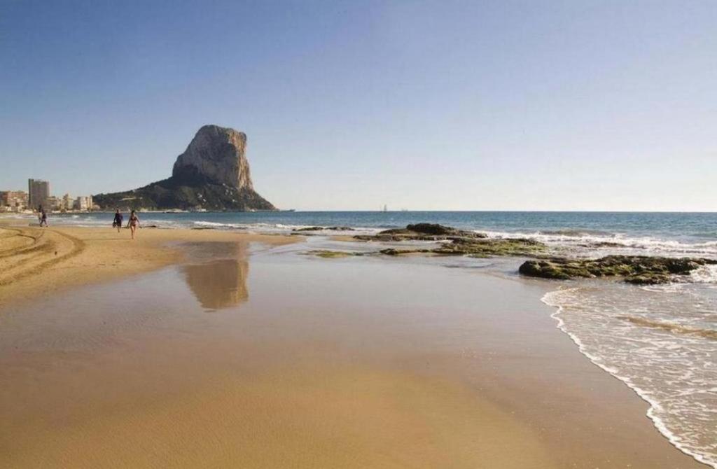 una spiaggia con una roccia nell'acqua e persone che camminano di FRONTIMAR a Calpe