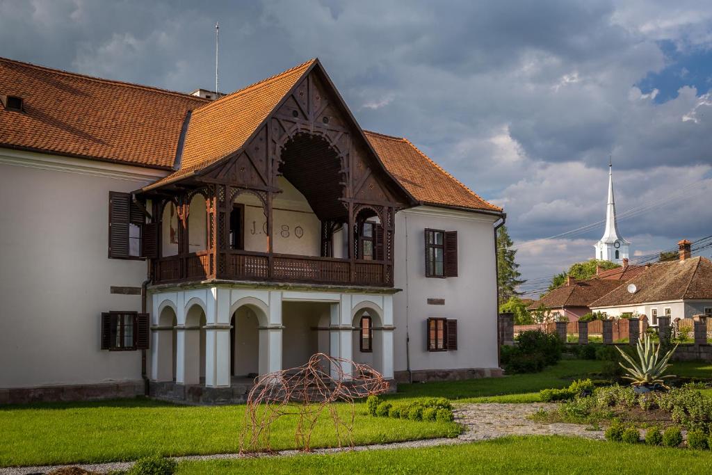 a white building with a brown roof and a church at Castle Hotel Daniel in Baraolt