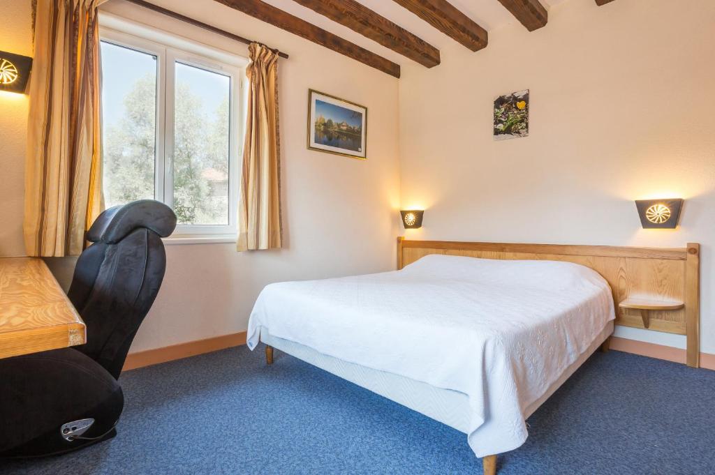 a bedroom with a bed and a chair and a window at Logis Hotel Restaurant Auberge Les Rives de l'Arzon in Vorey