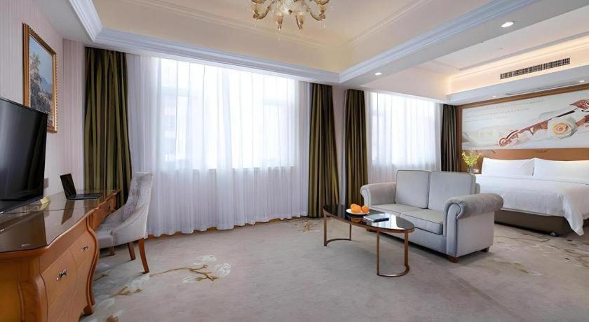 ein Hotelzimmer mit einem Bett, einer Couch und einem Fernseher in der Unterkunft Vienna Hotel Hebei Hengshui High-Speed Railway Station in Hengshui