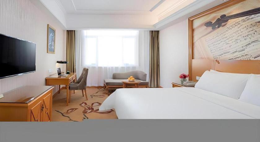 ein Hotelzimmer mit Bett, Schreibtisch und Fernseher in der Unterkunft Vienna Hotel Shanxi Datong High-Speed Railway Station Wanda Plaza in Shuiposhi